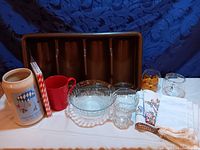 Photo showing assorted kitchen items including ceramic mugs, utensil tray, glass bowls, containers, and textiles