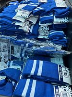 Stack and pile of multiple individually packaged blue athletic knee socks with white stripes and Create Loud! branded tags.