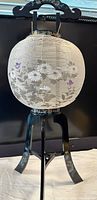 Mid-century Okinawa paper lantern lamp showing spherical paper shade with floral painting and black wooden curved frame with floral decoration.