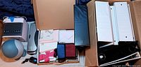 Wide view of box contents showing binders, staplers, card sets, and fabric pouches.