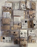 Top-down photo of numerous wooden block mounted rubber stamps, clear mounted sets, all in plastic cases, showing variety of floral and decorative designs