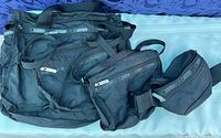 Four black LeSportsac travel bags of different sizes arranged on a blue patterned fabric surface to show set contents.