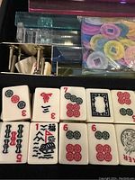 Close-up photo of the Mahjong tiles, acrylic tile holders, and colorful scoring chips inside the case.