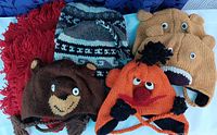Photo showing eight colorful winter beanies, including designs with bears, cartoon-like characters with pom-poms, patterned knit, and fleece-lined interiors