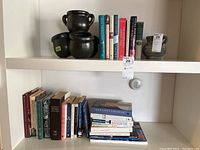 Two shelves of assorted books with vases on the upper shelf; books cover Canadian fiction, Canadiana, nature, travel, Downton Abbey and more.