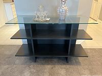 Front view of black wood veneer buffet with removable clear glass top. Shows three horizontal shelves.