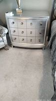 Front view of silver laminate dresser showing three drawers with square metal handles and curved front design.