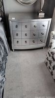 Front view of silver laminate 3 drawer dresser positioned between bed and armchair.