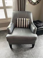 Front view of grey leather armchair with striped throw cushion on seat