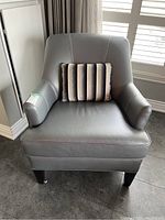 Front view of grey leather armchair with striped throw cushion on seat.