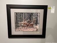 Framed print showing two deer in snowy, wooded winter landscape, double matted and behind glass in black composite frame approximately 19x22.5 inches.