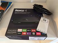 Roku 4 box with HDMI cable on top positioned on white surface.