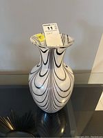 Front view of glass vase showing black and white swirl pattern and flared rim, sitting on a reflective surface.