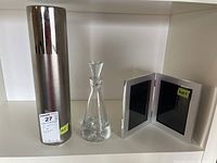 Lot including a metallic cylindrical ceramic vase, a clear glass Krosno decanter with stopper, and a folding double photo frame with metal edges.
