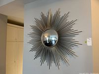 Front view of starburst metal wall decor with center round mirror showing the layered metal rods radiating outward.
