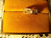 10K gold ring with four colored gemstones displayed on an orange textured surface, showing the ring's curved front and stones in red, clear, purple, and green hues.