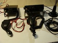 Two CB radios on a table, showing microphones, an antenna, and wiring for dash mounting.