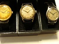 Photo showing all three watches side by side in black holders, Mercury on left, Bulova center, Birks right, highlighting dial designs and bands