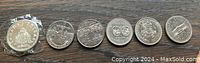 Photo of six Canadian commemorative silver dollar coins arranged in a row on a wooden surface, each with unique designs showcasing different Canadian historical or cultural events.