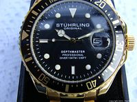 Close-up of the Stuhrling Original Depthmaster black dial and gold tone bezel and case, showing dial details and date window.