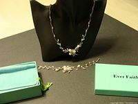 Necklace displayed on a black stand with matching bracelet alongside in green box and Ever Faith instruction or branding card.