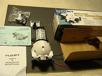 FloJet water pump with safety and installation instructions, packaging box, and additional fittings, new in box setup.