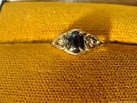 Close-up view of the ring face showing the dark oval stone and adjacent gold filigree detailing on a golden yellow textured background.