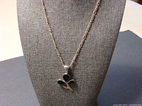 Front view of the necklace displayed on a stand showing the black rhinestone 3-leaf clover pendant attached to the silver chain.