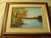 Framed landscape oil painting showing autumn trees and a lake under a clear sky.