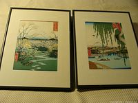 Two framed woodblock prints side by side on a beige textured surface showing traditional Japanese landscapes with Mount Fuji.