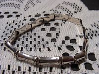 Full view of the sterling silver bamboo motif bracelet laid flat on a lace cloth showing the segments and clasp.