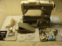 Full view of Pfaff 360 sewing machine on stand with accessories including power cord, foot pedal, instruction manuals, thread discs, bobbins, needles, and sewing parts.