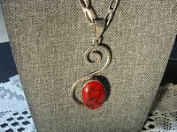 Front view of silver pendant with red stone on chain against fabric background