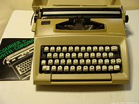 Front angle view of beige Smith Corona Courier portable typewriter, showing keyboard and manual on the left side.