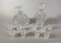 Full lot of 2 cut crystal decanters and 9 shot glasses arranged on surface