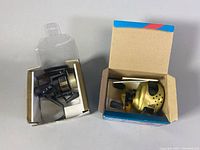 Two fishing reels in original boxes side by side. Left is Daiwa PM1300H spinning reel, right is Abu Garcia Ambassadeur Gold Max bait casting reel in blue box.