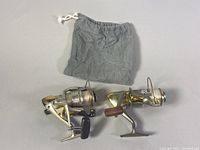 Two fishing reels laid flat next to a gray drawstring pouch, showing overall condition and included pouch.