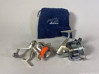Both fishing reels displayed side by side with Okuma pouch in background.
