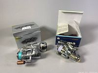 Both bait cast reels displayed with their original boxes; Shimano BB-X 3000-T box is silver with 'SHIP' and model text; OKUMA Epixor EF20 box is blue with model info.