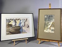Two framed watercolor paintings side by side on wooden easels, one depicting kitchen bowls scene, the other a winter house scene
