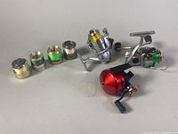 Three spinning reels (red palm reel, silver reels with gold and green spools) next to three spare spools pre-spooled with line