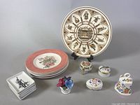 Full view of all items arranged on grey background: Wedgwood Shakespeare plate on a stand, stacked coral rimmed plates, small trinket boxes, porcelain flowers, small rectangular plates