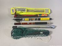 Fishing rod, carrying case, additional metal rod section and green bait net/trap viewed together.