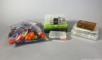Photo showing all items including a sealed bag of assorted fishing lures, bobbers, hooks, and six plastic storage bins in various colors and sizes