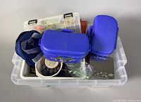 Top-down photo of clear plastic storage bin containing multiple fishing tackle boxes and containers in blue, white, and transparent colors.