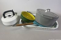 Full view of all items in the lot showing teapot, green-yellow pan, gray cast iron casserole with lid, and rectangular enamel roasting pan.