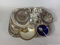Top-down view of stacked silver trays, pedestal dish, cobalt blue glass bowl, and small silver serving items on large rectangular tray.