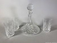 Decanter with stopper and three lowball glasses arranged in front of white background
