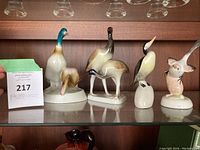 Front view of five porcelain bird figurines arranged on glass shelf under light with auction card visible