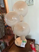 Front view of lamp showing base and three white globe shades